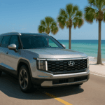 2025 Hyundai Santa Fe driving along Florida's Gulf Coast, with palm trees, white sandy beaches, and turquoise ocean in the background under a clear blue sky.