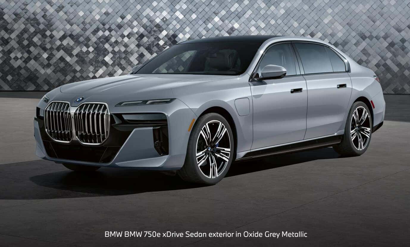 BMW 750e xDrive Sedan exterior in Oxide Grey Metallic on a modern concrete courtyard.