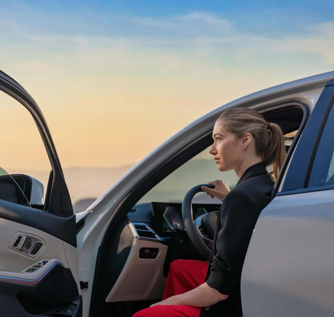 A woman sits inside a BMW 3 Series car with the driver’s side door open