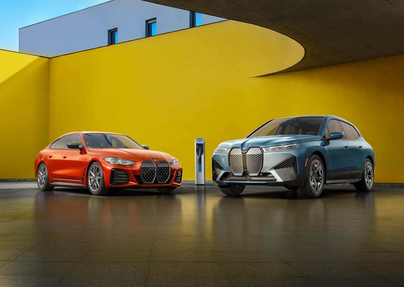 BMW Certified iX and i4 parked at a charging station in front of a colorful building wall
