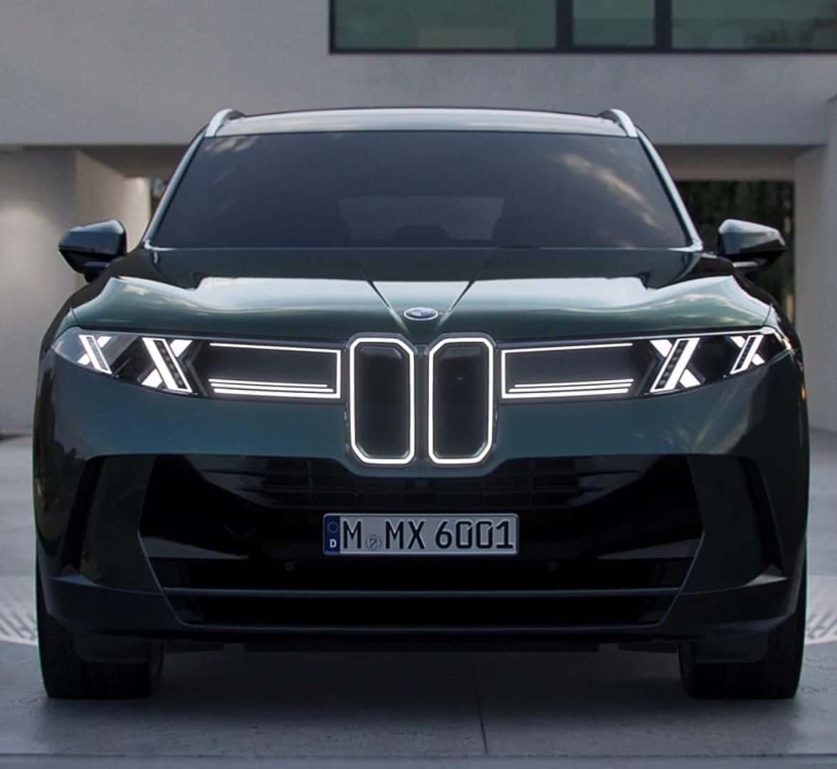 Front view of a dark green BMW X5 parked outside a modern home with illuminated LED headlights.