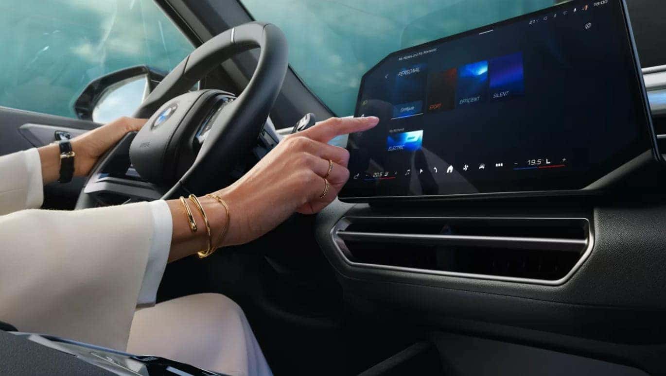 Driver using the BMW X5 touchscreen infotainment display to adjust vehicle settings inside the cabin.