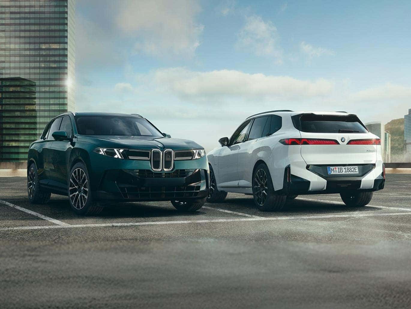 Dark green and white BMW X5 models parked side by side in an urban setting with modern buildings in the background.
