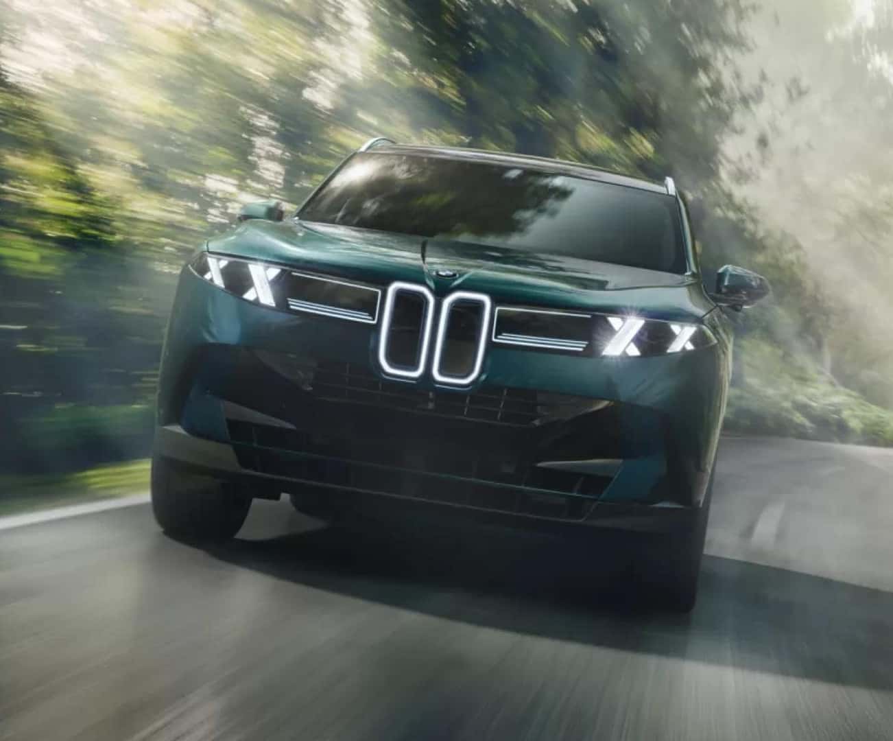 Dark green BMW X5 driving along a forest road with illuminated LED headlights and motion blur in the background.