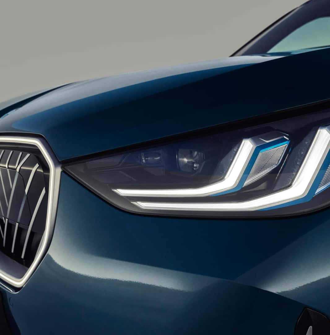 Front close-up view of blue BMW X3 LED headlight and grille against grey background.