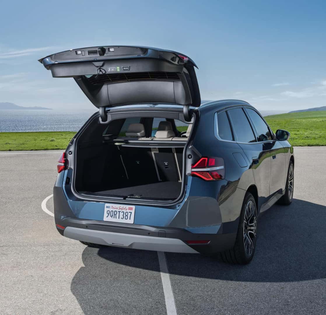 Rear three-quarter view of blue BMW X3 with open trunk parked near ocean overlook.