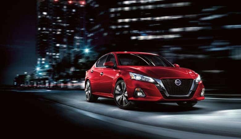 A red 2019 Nissan Altima driving at night in the city - Bert Ogden Nissan in McAllen, TX