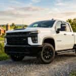White Chevrolet Silverado pickup truck parked on a gravel path in front of a farm at sunset.