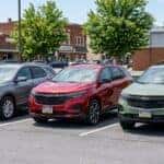 Three Chevrolet Equinox SUVs in silver, red, and green parked in a row in a small town parking lot.