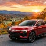 Red Chevrolet Blazer EV parked on a scenic overlook during a mountain sunset with autumn foliage.