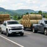 A photorealistic 2026 Chevrolet Silverado 1500 and 2500HD pulling a trailer of hay on the highway in pennsylvania