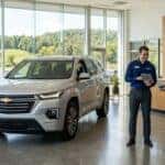A silver Chevrolet SUV in a modern dealership showroom with a salesperson assisting a customer.