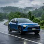 Blue Chevrolet Blazer EV driving along a wet, winding mountain road surrounded by misty green forests. (Representative image for illustration purposes only. Actual vehicle may vary based on trim and configuration.)