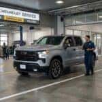A service advisor talking to a customer in a silver Chevrolet Silverado truck inside a modern service center drive. (Representative image for illustration purposes only. Actual vehicle may vary based on trim and configuration.)