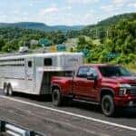 A red Chevrolet Silverado dually truck towing a silver livestock trailer on a highway. (Representative image for illustration purposes only. Actual vehicle may vary based on trim and configuration.)