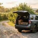 A grey SUV with an open trunk filled with wooden crates parked on a dirt path in a sunny apple orchard. (Representative image for illustration purposes only. Actual vehicle may vary based on trim and configuration.)