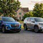A blue Chevrolet Traverse and a silver Honda Pilot parked side by side in a paved driveway in front of a suburban home. (Representative image for illustration purposes only. Actual vehicle may vary based on trim and configuration.)