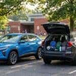 A bright blue Chevrolet SUV and a dark grey SUV with an open trunk full of backpacks in a school parking lot. (Representative image for illustration purposes only. Actual vehicle may vary based on trim and configuration.)