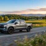 A grey pickup truck driving on a winding country road past farmland at sunset. (Representative image for illustration purposes only. Actual vehicle may vary based on trim and configuration.)
