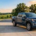 A dark blue GMC Sierra Denali pickup truck parked outside an automotive service building during golden hour. (Representative image for illustration purposes only. Actual vehicle may vary based on trim and configuration.)