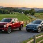A red Chevy Silverado truck and a blue Chevy Equinox EV parked on a rural road at sunset. (Representative image for illustration purposes only. Actual vehicle may vary based on trim and configuration.)