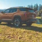 Bronze Chevrolet Equinox SUV parked near a lake with a mother and child running on the grass.