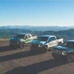 Three Chevrolet Silverado pickup trucks in green, silver, and black parked on a mountain scenic overlook.