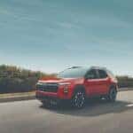 Red Chevrolet Equinox RS SUV driving along a paved road under a clear sky.