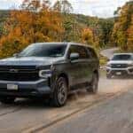A dark gray Chevrolet SUV driving on a winding road with autumn trees, followed by a silver Ford Expedition. (Representative image for illustration purposes only. Actual vehicle may vary based on trim and configuration.)