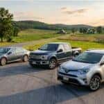 A gray sedan, blue pickup truck, and silver SUV parked on an asphalt pullout along a rural country road. (Representative image for illustration purposes only. Actual vehicle may vary based on trim and configuration.)