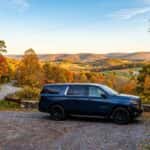 Dark blue SUV parked at a gravel scenic overlook surrounded by colorful autumn foliage and rolling hills. (Representative image for illustration purposes only. Actual vehicle may vary based on trim and configuration.)