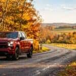 A red Chevrolet pickup truck driving down a winding rural road lined with vibrant yellow and orange autumn trees. (Representative image for illustration purposes only. Actual vehicle may vary based on trim and configuration.)