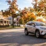 A silver Toyota RAV4 SUV parked along a curb on a suburban street framed by colorful autumn trees. (Representative image for illustration purposes only. Actual vehicle may vary based on trim and configuration.)