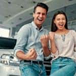 A happy couple is celebrates the great customer service they received in front of their new car.