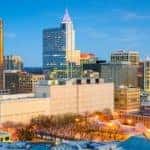 The Raleigh, NC, skyline is shown in front of a blue sky.