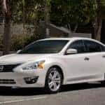 A white 2015 used Nissan Altima is shown from the front parked on the street angled left.