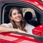 A woman is smiling inside a red car.