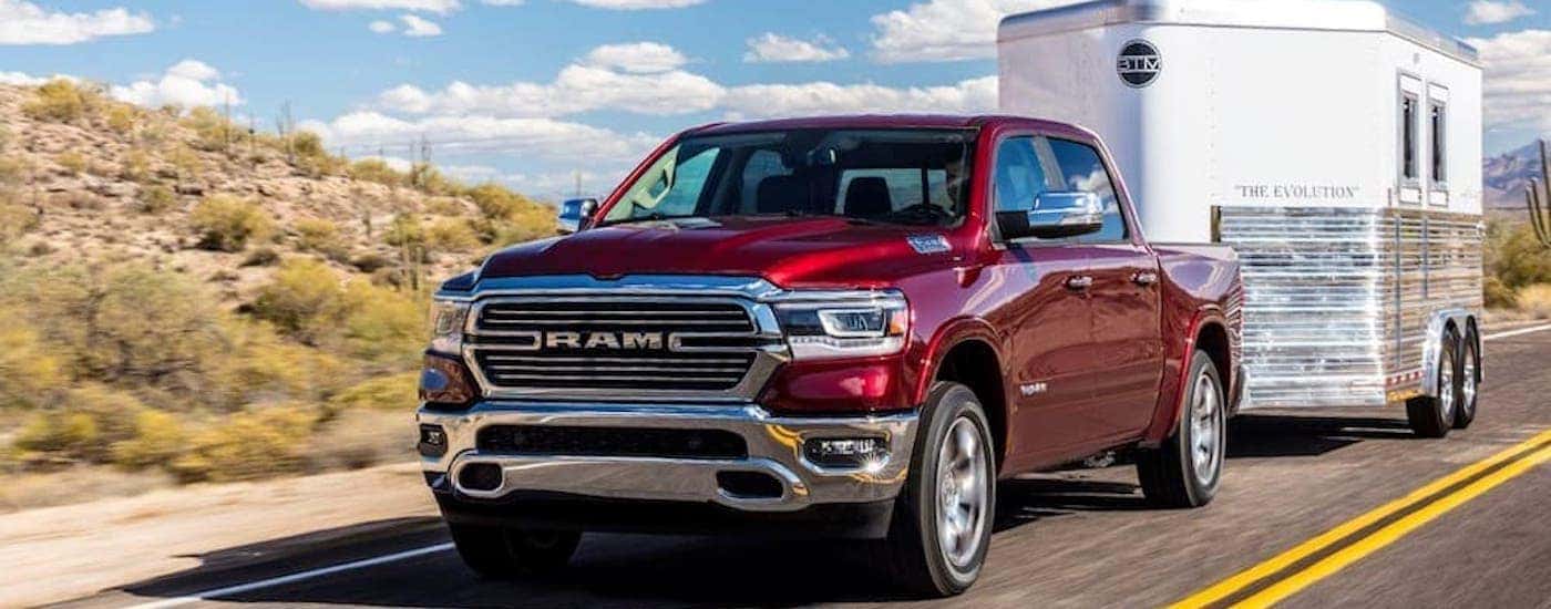 A red 2019 Ram 1500 is shown towing a trailer down an open road in the desert.