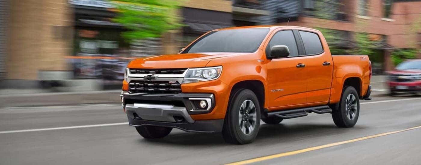 An orange 2021 Chevy Colorado is shown from the front driving through a city.