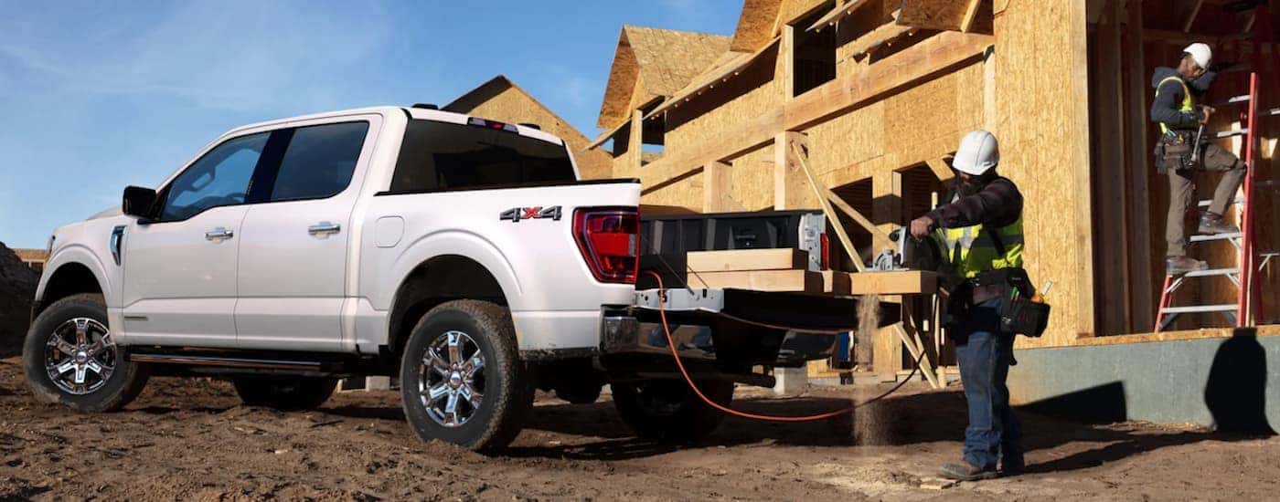 A white 2021 Ford F-150 is shown from the side parked in front of a construction site after leaving a used truck dealership.