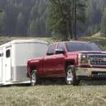 A red 2015 Chevy Silverado 1500 is shown towing a white trailer.