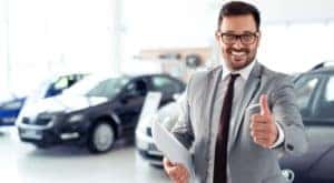 A man is giving a thumbs up at a car dealership.