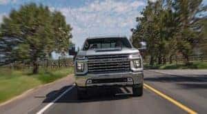 A silver 2020 Chevy Silverado 2500 HD Z71 is shown driving on a tree lined road.