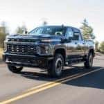 A grey 2020 Chevy Silverado 2500HD is shown from the front at an angle while it drives down the road after the owner searched 'used truck sales near me'.
