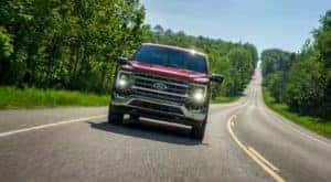 A popular used f-150 near you, a maroon 2021 Ford F-150, is shown driving on a tree-lined road.