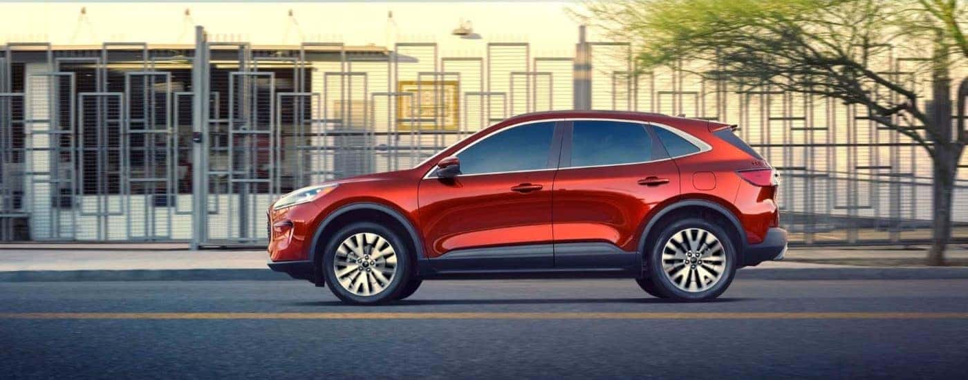 A red 2020 Ford Escape driving past modern architecture on a city street