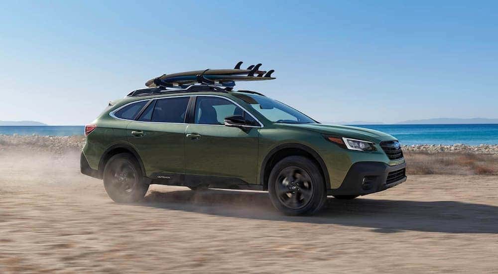 A green 2021 Subaru Outback is shown driving near an ocean.