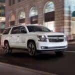A white 2020 Chevy Suburban is shown driving on a city street after viewing used SUVs Near Cary, NC.