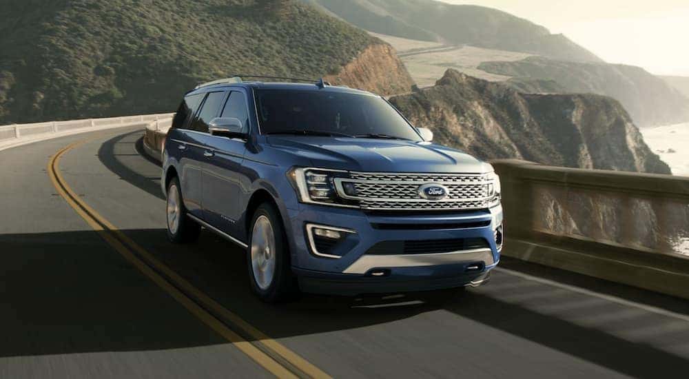 A blue 2020 Ford Expedition is shown driving near an ocean.