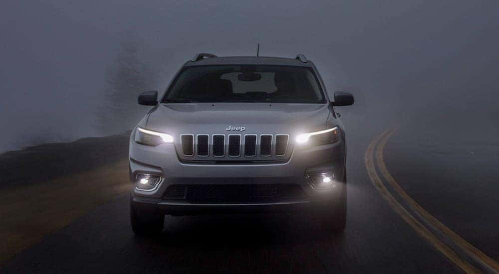 A silver 2020 Jeep Cherokee is shown driving through the fog.